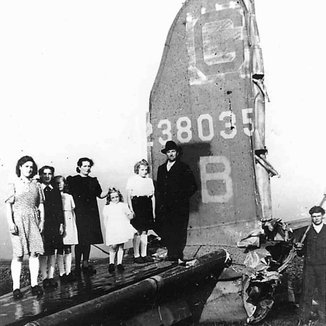 A Belgian family poses on the horizontal stabilizer of the severed tail of the B-17 bomber that fell in their farmyard (with Joe Jones inside it). (Source: 385th Bomb Group)